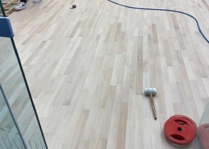 Een houten vloer die professioneel geschuurd wordt, met gereedschappen zoals een hamer en een schuurmachine zichtbaar op de vloer, tijdens een renovatieproject door Vloerenonderhoud Nederland.